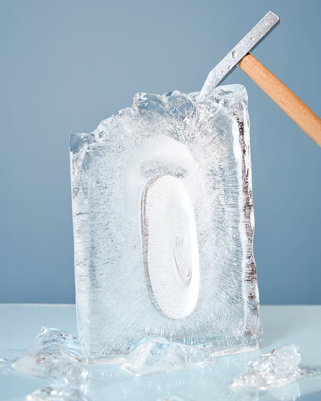 Cooling Roller in einem Eisblock eingefroren, der mit einem Hammer zerschlagen wird, wobei Eissplitter herunterfallen.