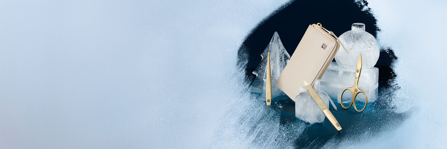 Vereiste an einer Stelle freigekratzt. Hier sind ein beiges Etui und goldene Maniküreprodukte, arrangiert auf weihnachtlichen Eisfiguren vor dunkelblauem Hintergrund.