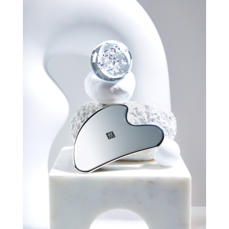 Darstellung des ZWILLING Premium Edelstahl-Gesichtsmassagers inmitten von artifiziellen Kunstobjekten.