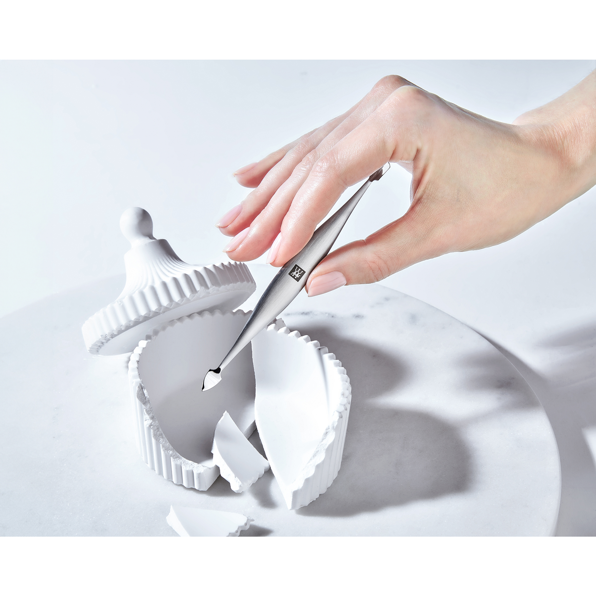 Sehr hochwertige Darstellung des ZWILLING Premium Nagelhautschiebers und -reinigers, welcher von einer Hand gehalten wird.