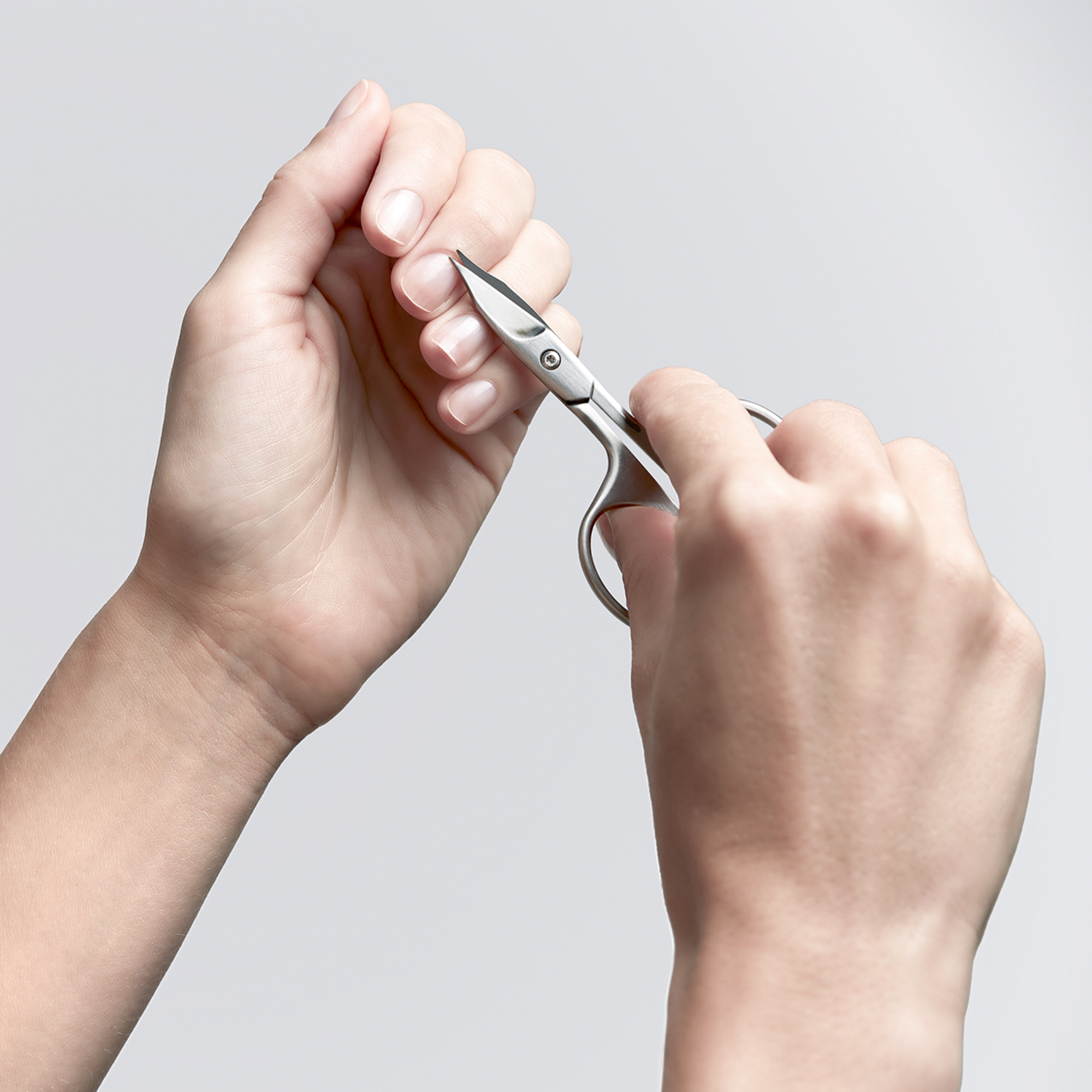 Anwendung einer ZWILLING Premium Nagel- und Nagelhautschere aus rostfreiem Edelstahl an der Nagelhaut des linken Mittelfingers.
