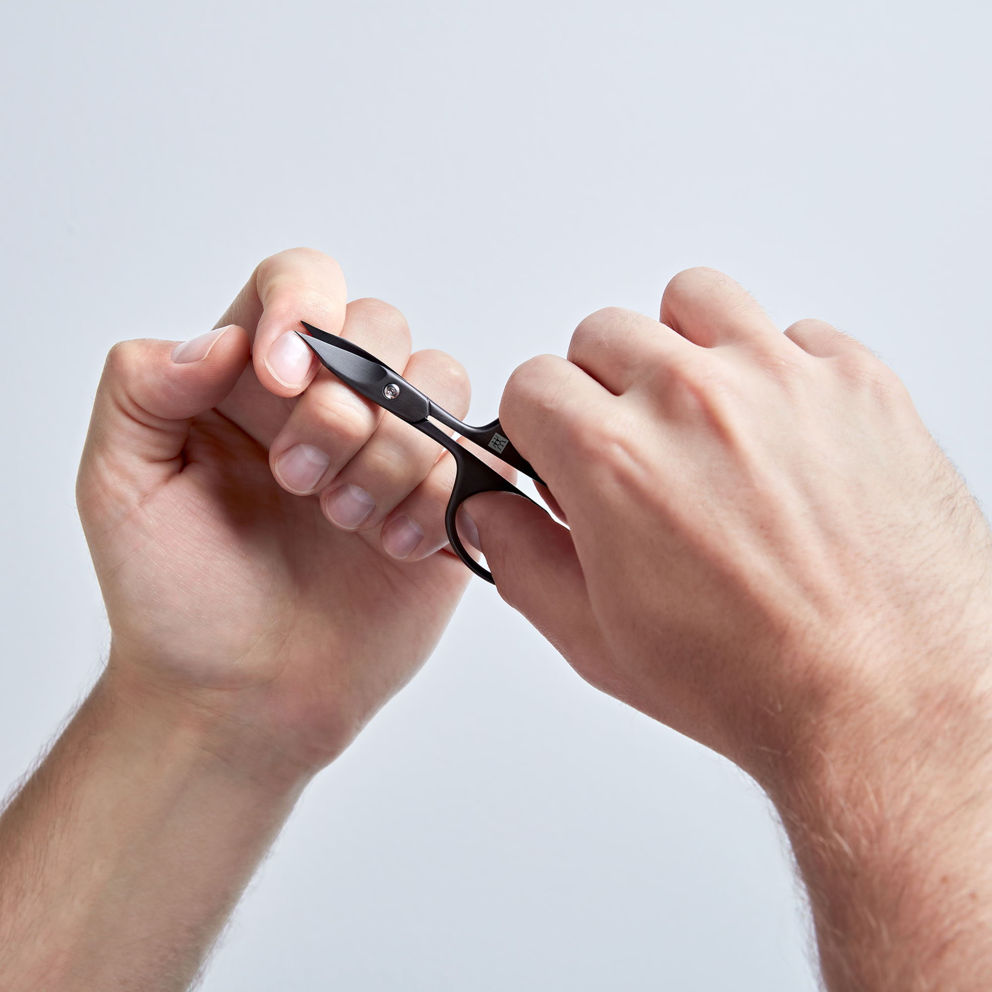 Anwendung einer ZWILLING Premium Nagel- und Nagelhautschere in Schwarz am linken Zeigefinger Nagel.