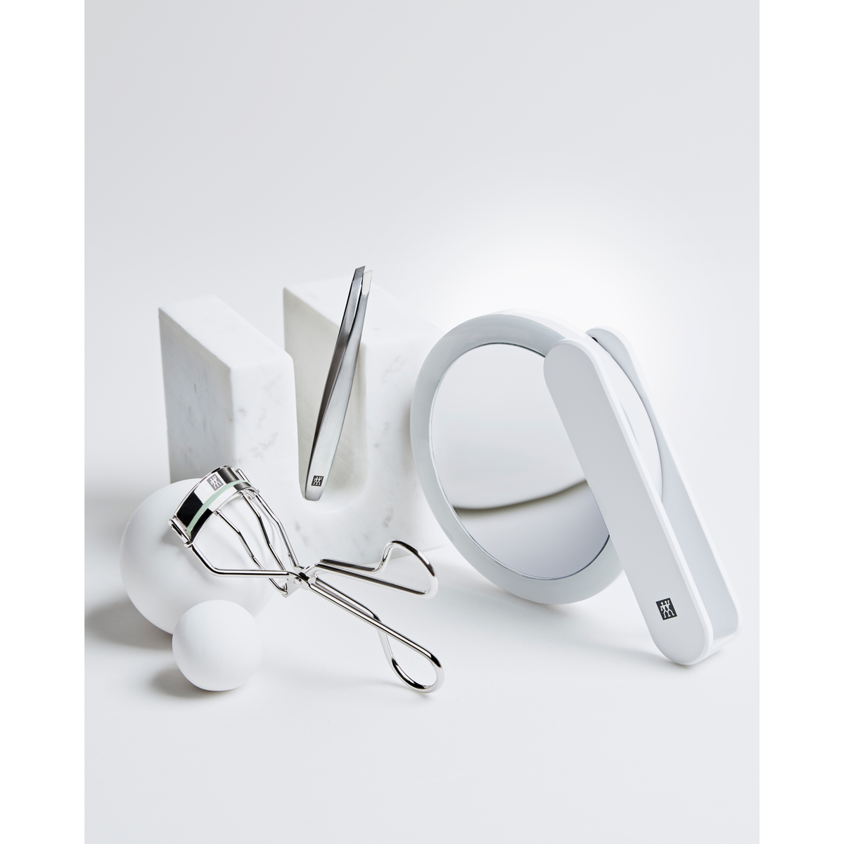 Darstellung des ZWILLING Premium LED-Kosmetikspiegels zusammen mit weiteren ZWILLING Produkten inmitten von artifiziellen Marmorobjekten.