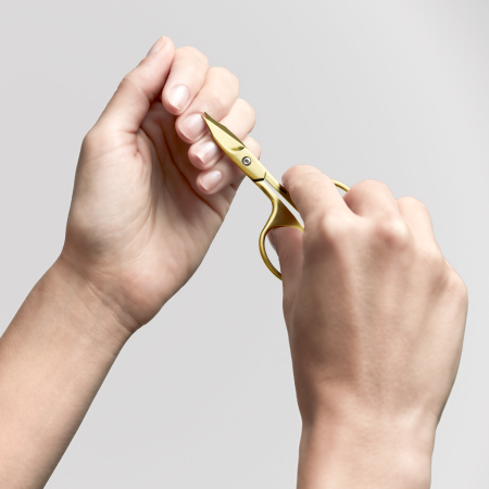 Anwendung einer ZWILLING Premium Nagel- und Nagelhautschere in Gold an der Nagelhaut des linken Mittelfingers.