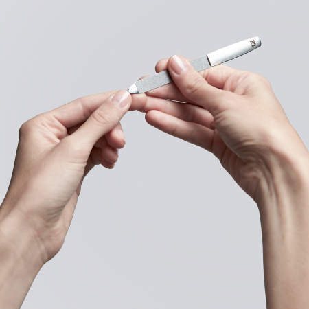 Anwendung der Spitze einer ZWILLING Premium Saphir-Nagelfeile aus rostfreiem Edelstahl unterhalb des linken Daumennagels.