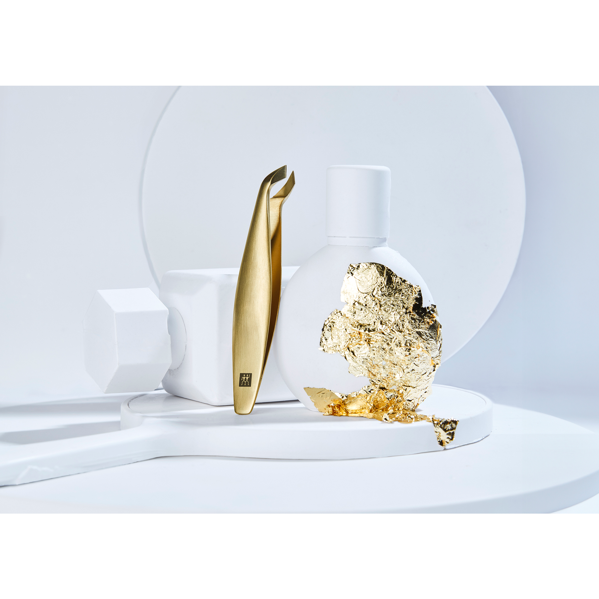 Darstellung des ZWILLING Premium Nagelhautschneiders in gold neben artifiziellen Keramikobjekten und Blattgold als Kontrast.