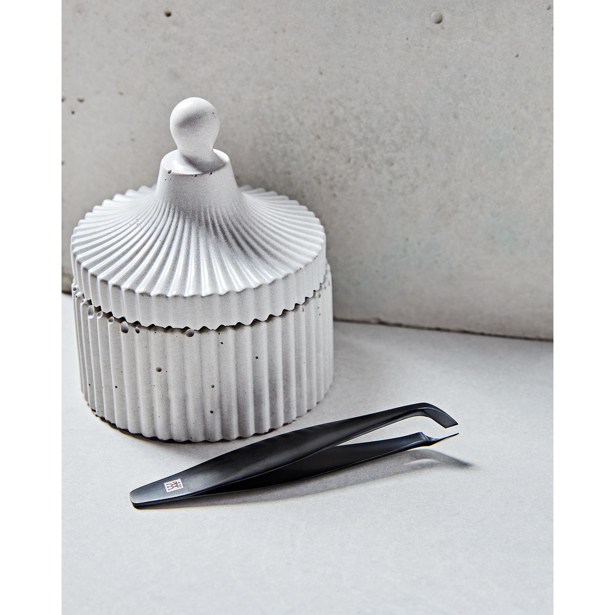 Darstellung des ZWILLING Premium Nagelhautschneiders in schwarz neben artifiziellen Betonobjekten.