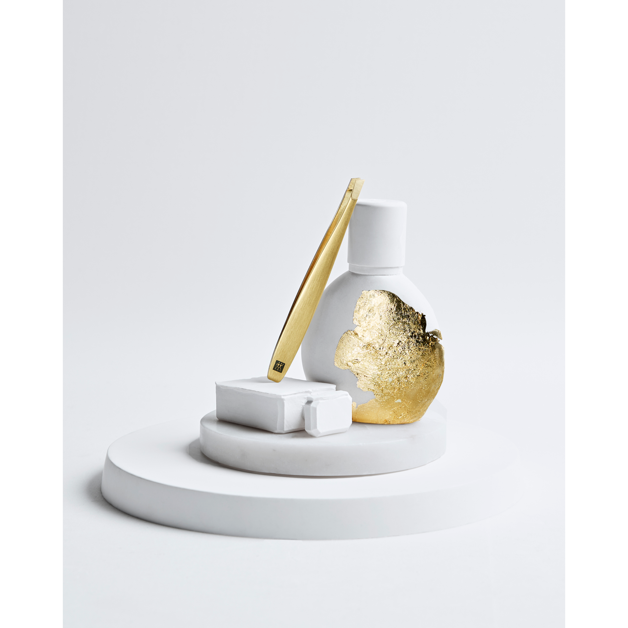 Darstellung der ZWILLING Premium Pinzette, schräg in Gold, liegend auf artifiziellen Objekten, mit Blattgold veredelt.