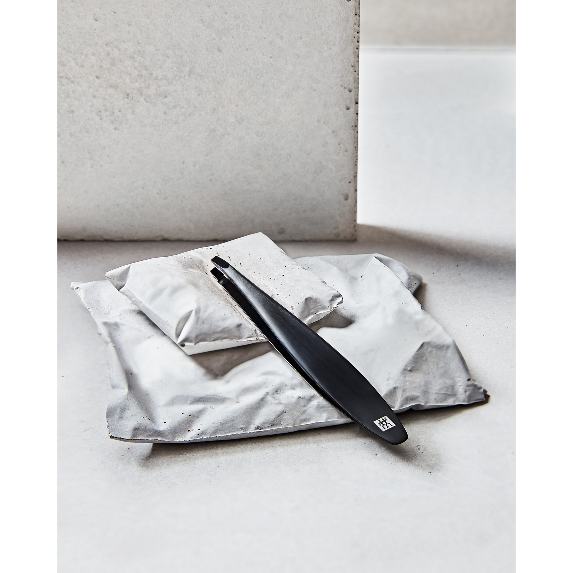 Darstellung der ZWILLING Premium Pinzette, schräg in Schwarz, liegend auf artifiziellen Betonobjekten.