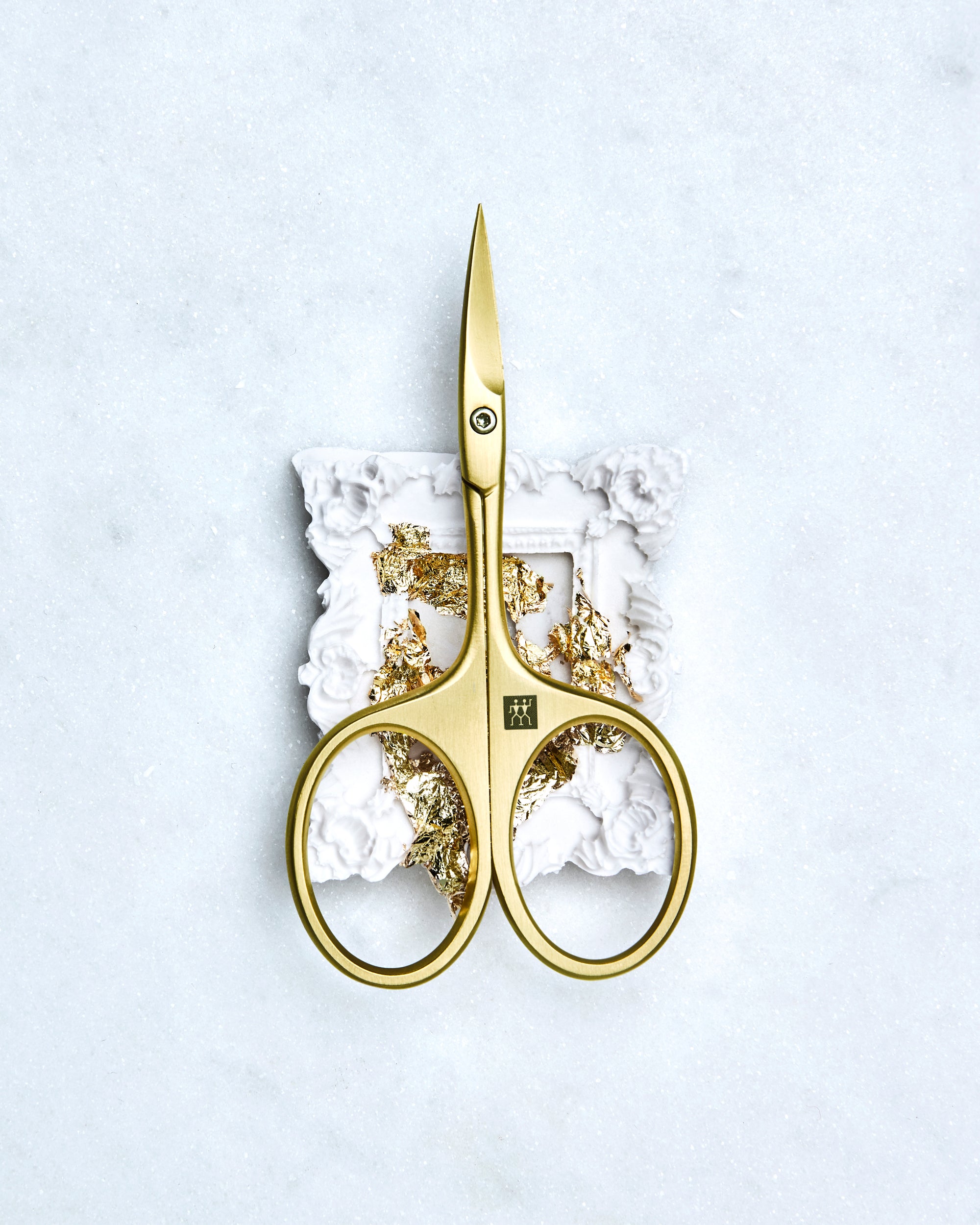 Sehr hochwertige Darstellung der ZWILLING Premium Nagelhautschere inmitten eines artifiziellen Rahmens mit Blattgold.