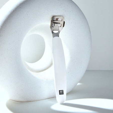 Darstellung des ZWILLING Premium Hornhauthobels in weiß vor einem runden Steinobjekt mit Loch.