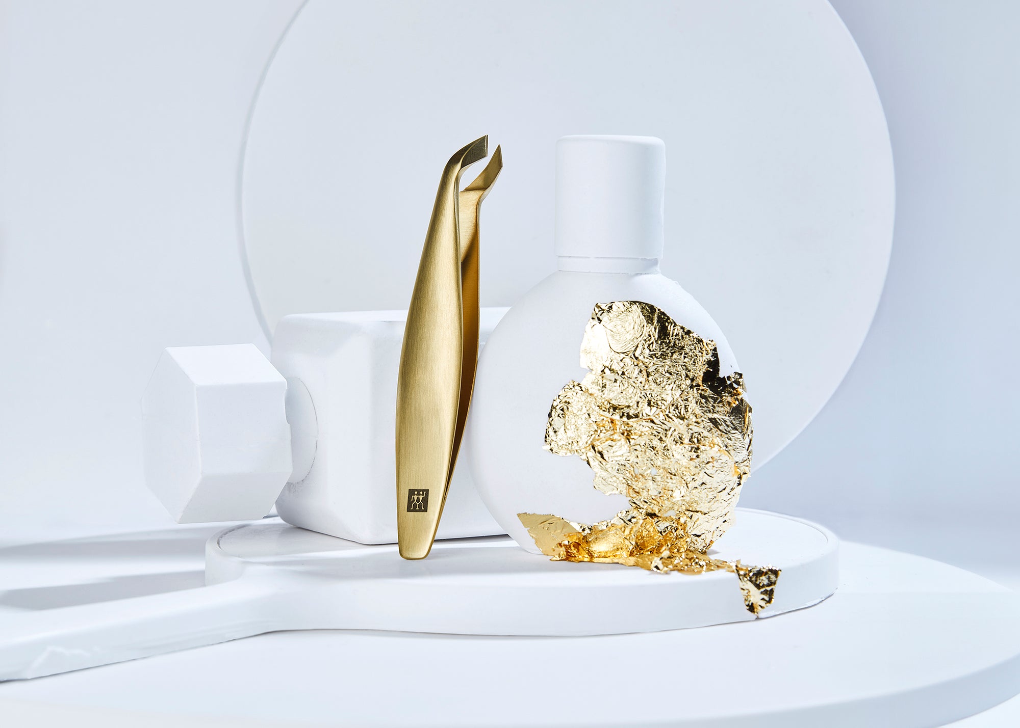 Darstellung des ZWILLING Premium Nagelhautschneiders in gold neben artifiziellen Keramikobjekten und Blattgold als Kontrast.
