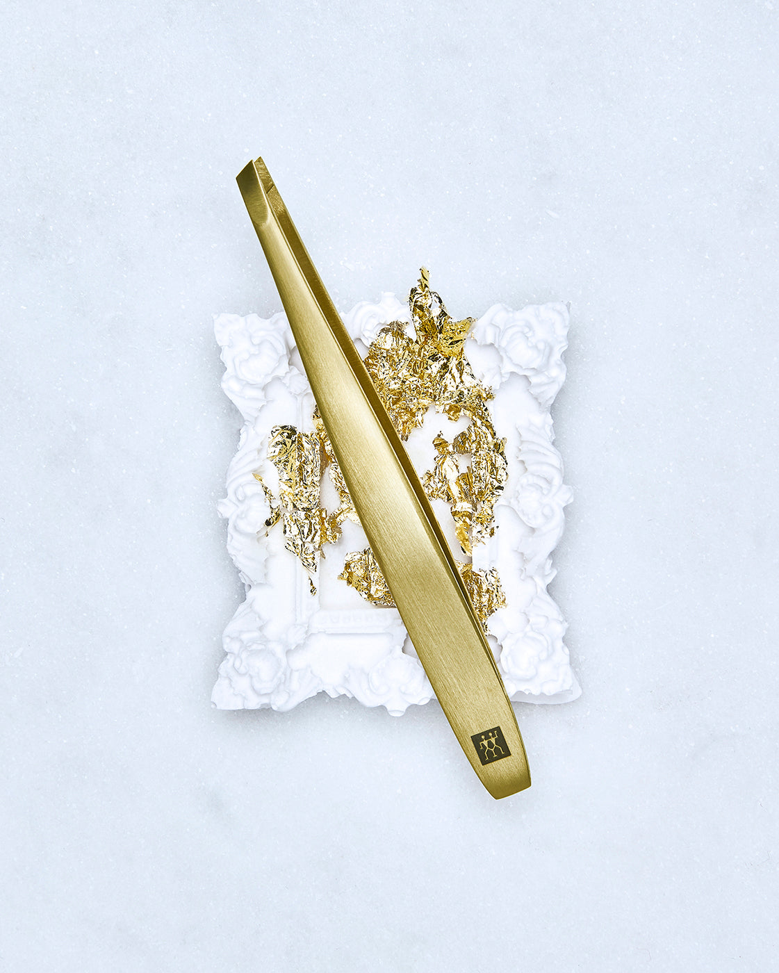 Darstellung der ZWILLING Premium Pinzette, schräg in Gold, liegend auf artifiziellen Objekten, mit Blattgold veredelt.