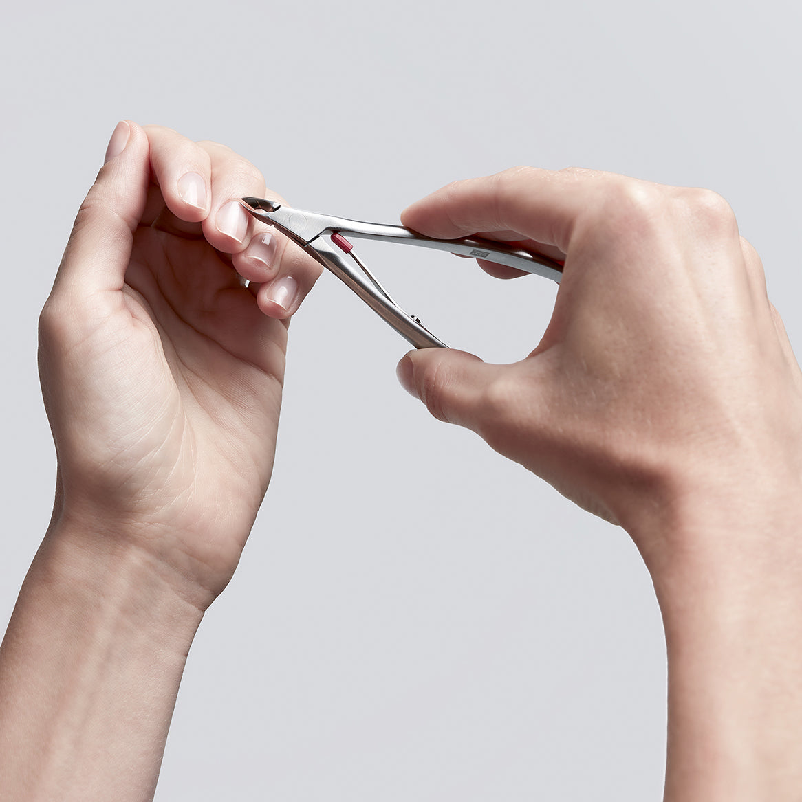 Anwendung einer ZWILLING Premium Nagelhautzange aus rostfreiem Edelstahl an der Nagelhaut des linken Mittelfingers.
