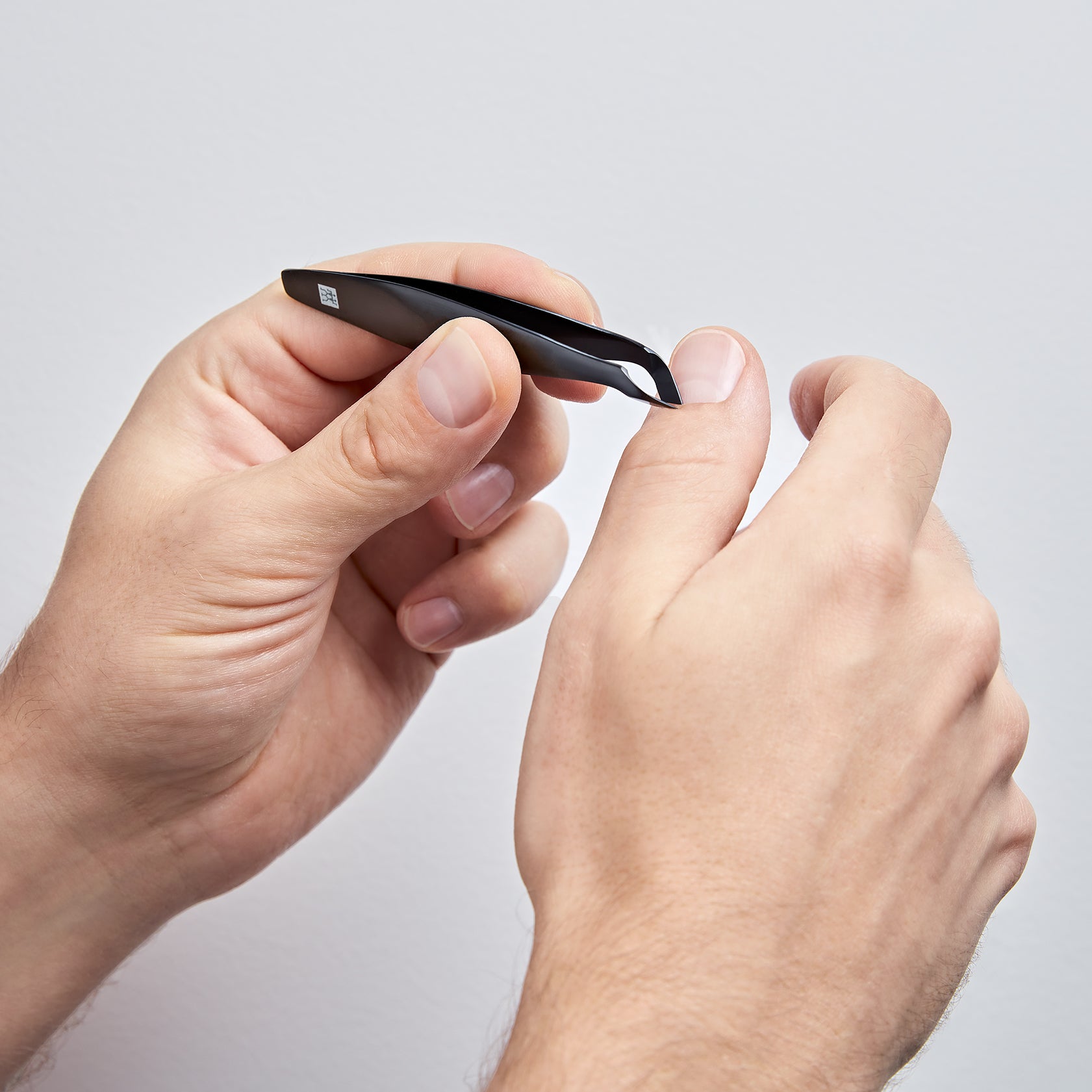 Anwendung eines ZWILLING Premium Nagelhautschiebers in schwarz an der Nagelhaut des rechten Daumens.