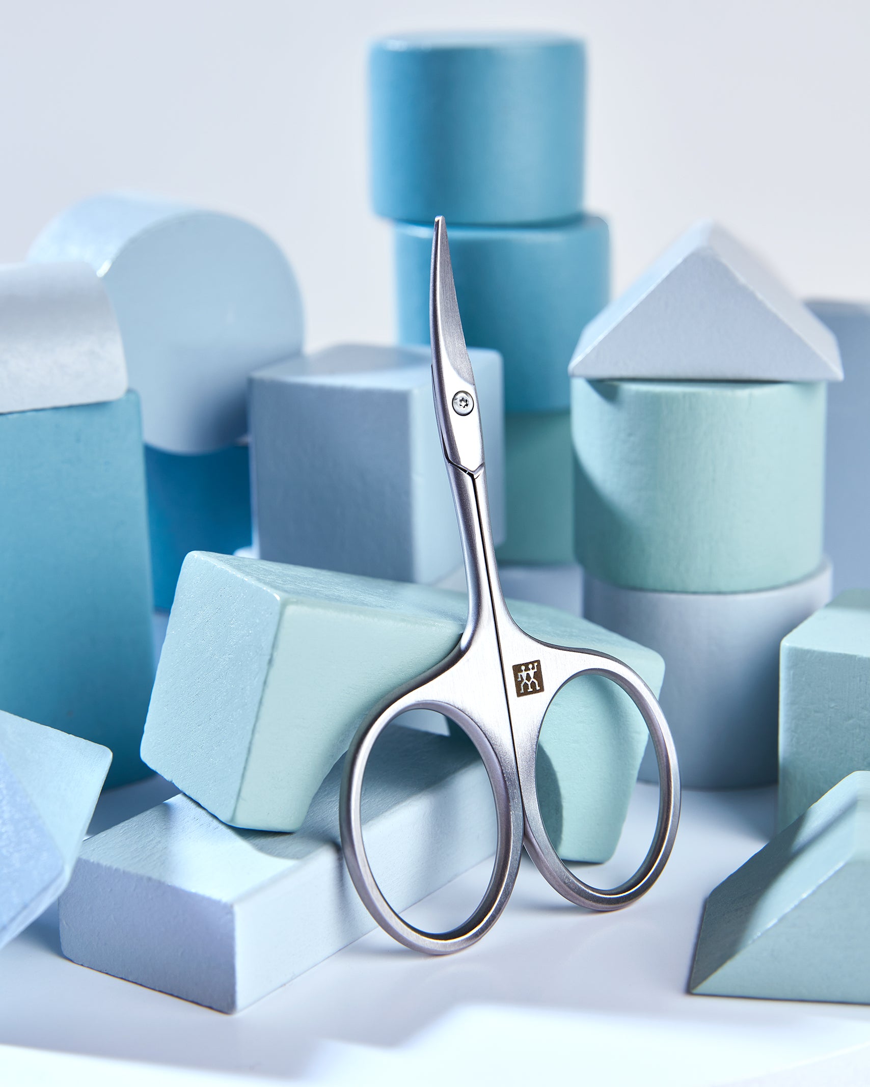 Sehr hochwertige Darstellung der ZWILLING Premium Baby-Nagelschere inmitten von blauen, verspielten Holzobjekten.