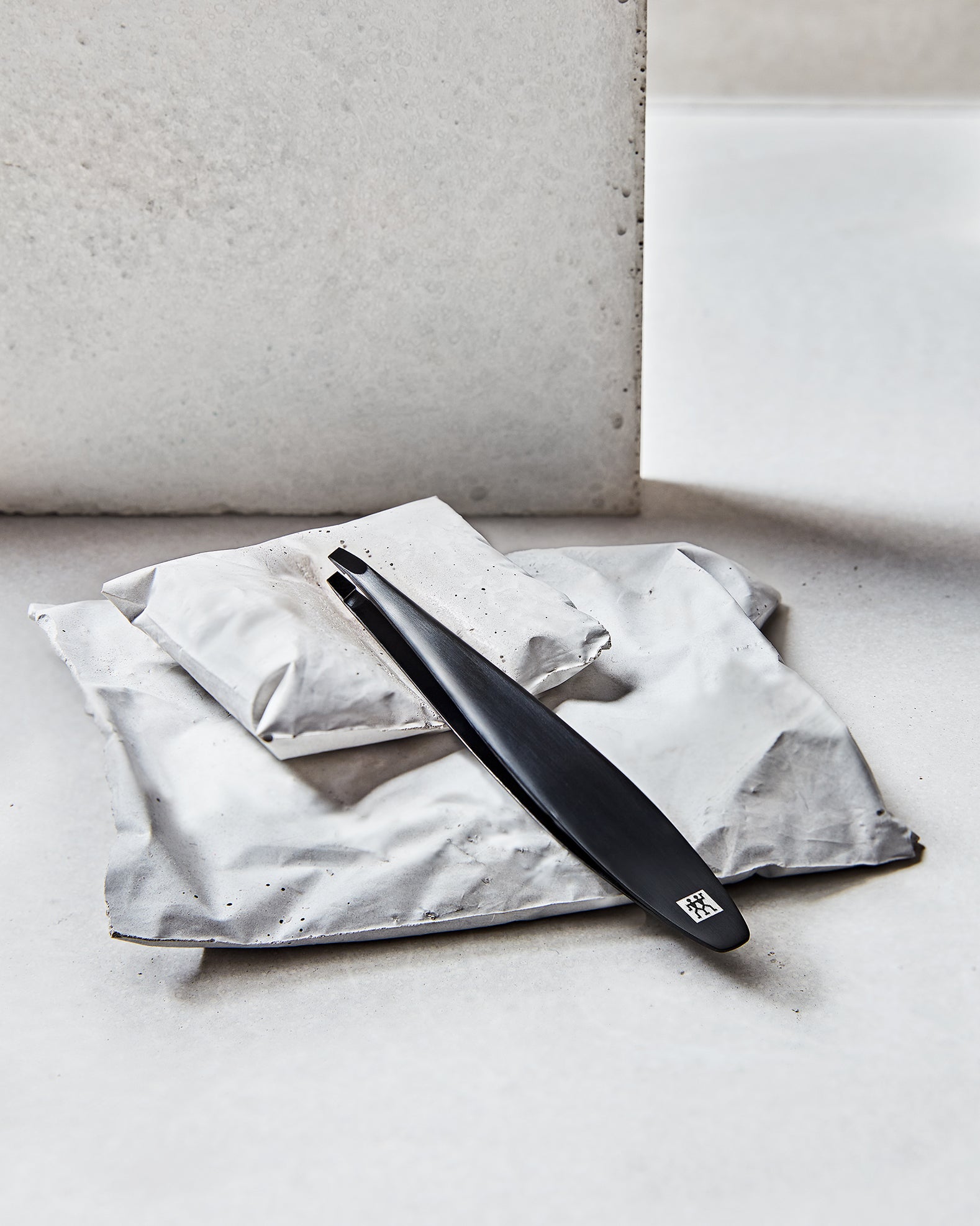 Darstellung der ZWILLING Premium Pinzette, schräg in Schwarz, liegend auf artifiziellen Betonobjekten.