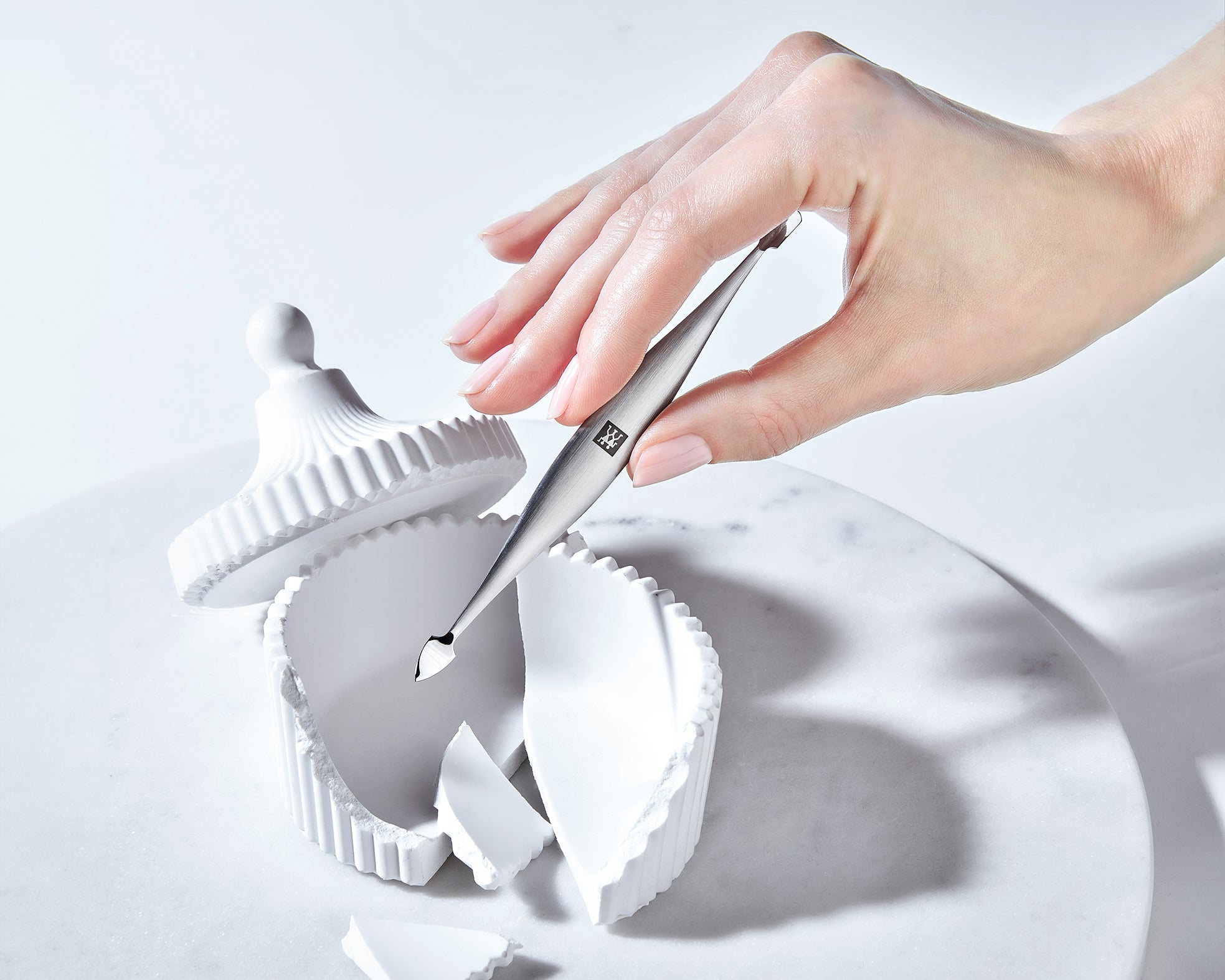 Sehr hochwertige Darstellung des ZWILLING Premium Nagelhautschiebers und -reinigers, welcher von einer Hand gehalten wird.