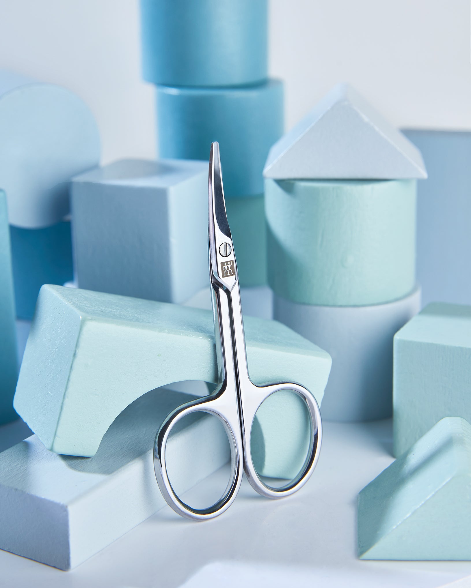 Sehr hochwertige Darstellung der ZWILLING Classic Baby-Nagelschere inmitten von blauen, verspielten Holzobjekten.