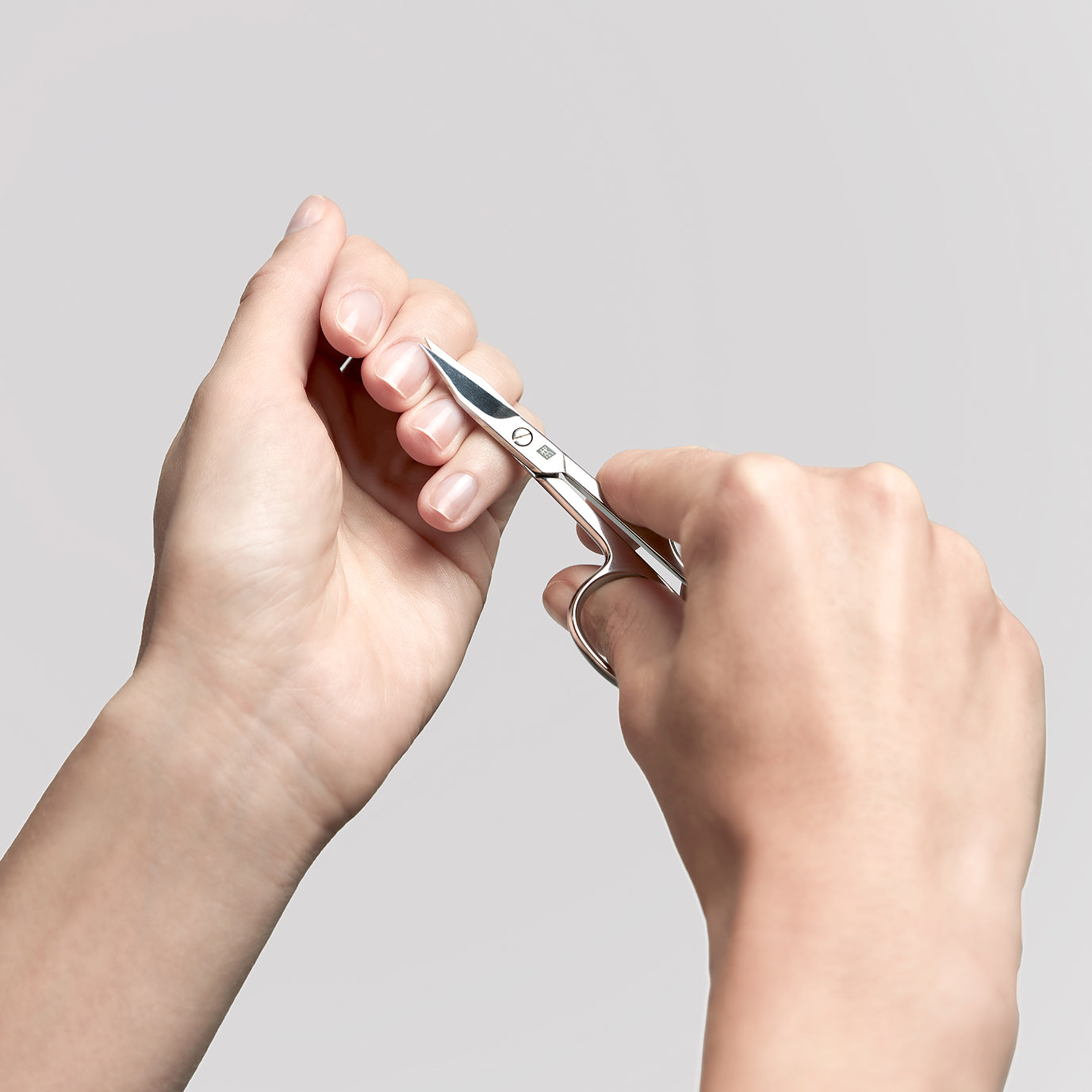 Anwendung einer ZWILLING Classic Nagel- und Nagelhautschere aus rostfreiem Edelstahl an der Nagelhaut des linken Mittelfingers.