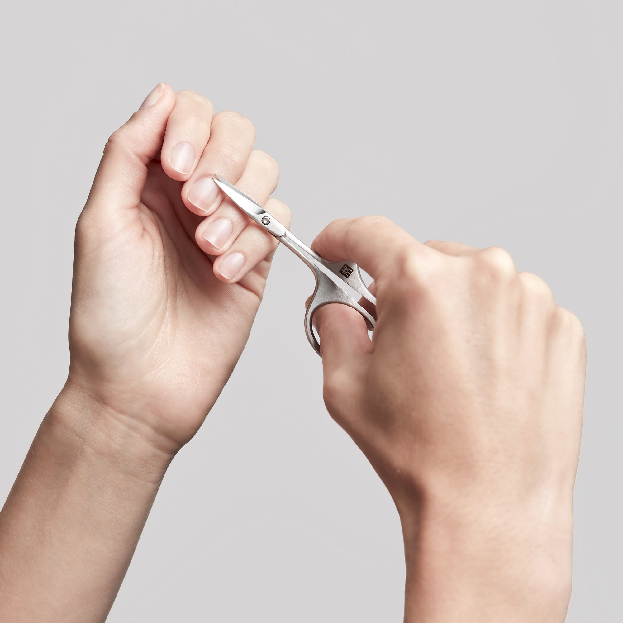 Anwendung einer ZWILLING Premium Nagelhautschere aus rostfreiem Edelstahl an der Nagelhaut des linken Mittelfingers.