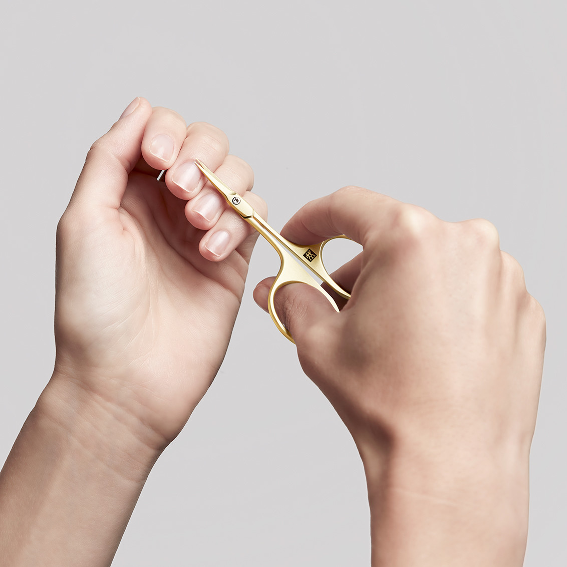 Anwendung einer ZWILLING Premium   Nagelhautschere aus Gold an der Nagelhaut des linken Mittelfingers.